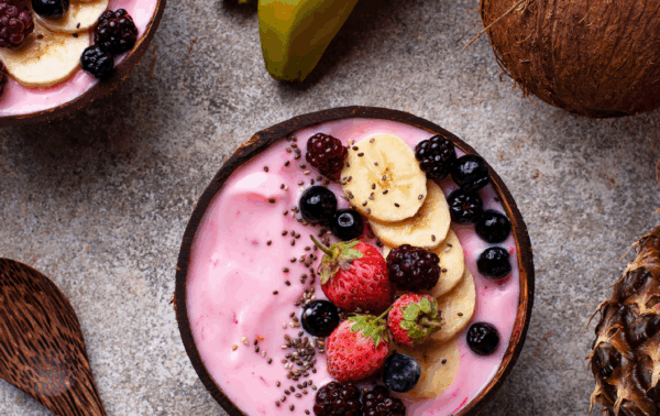 Deux bols de nice cream au fruit rouge à côté d'une noix de coco, d'un ananas et de bananes
